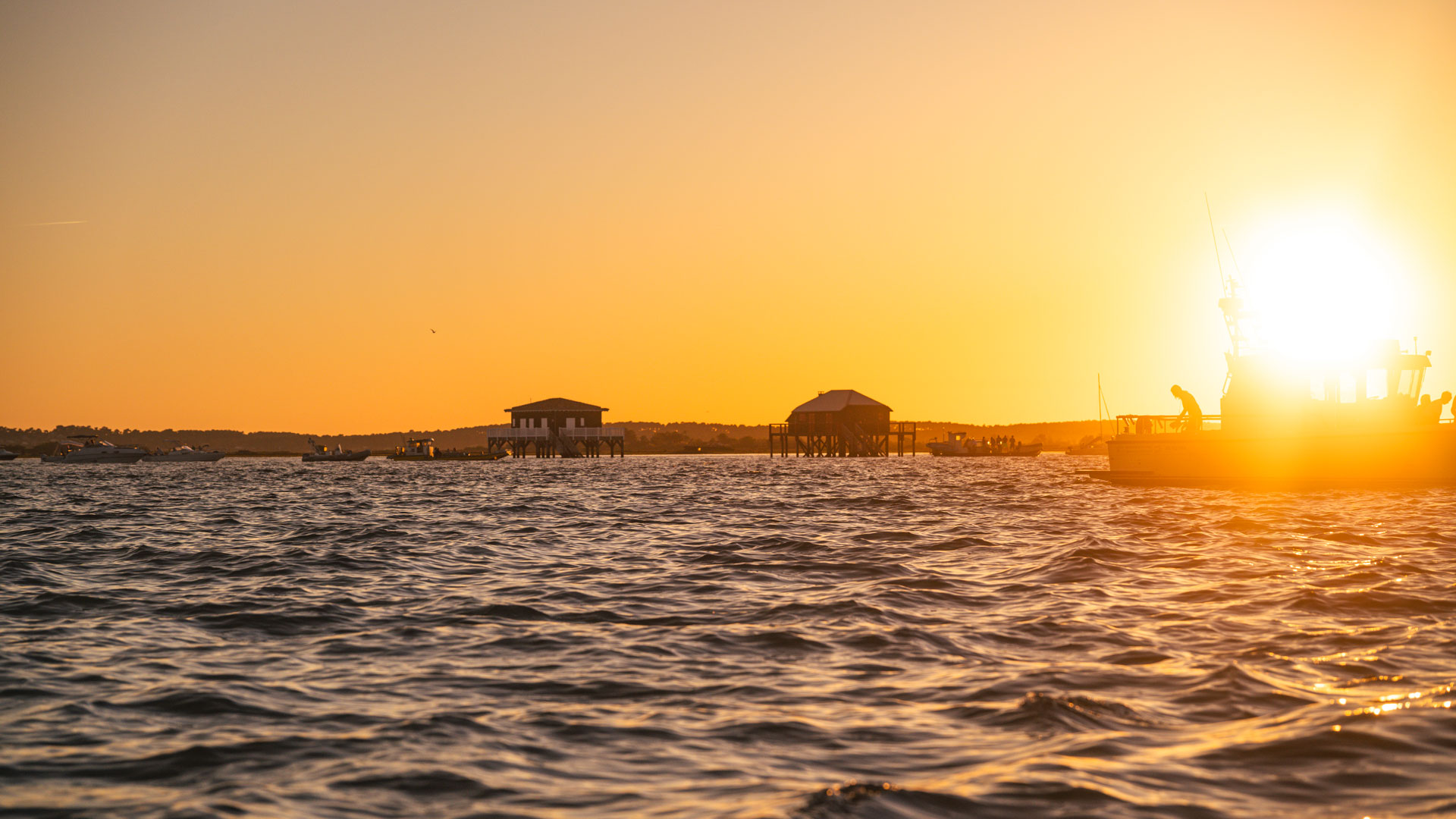 Cabanes Tchanquées sur pilotis au coucher de soleil sur le Bassin d’Arcachon, vues depuis un bateau