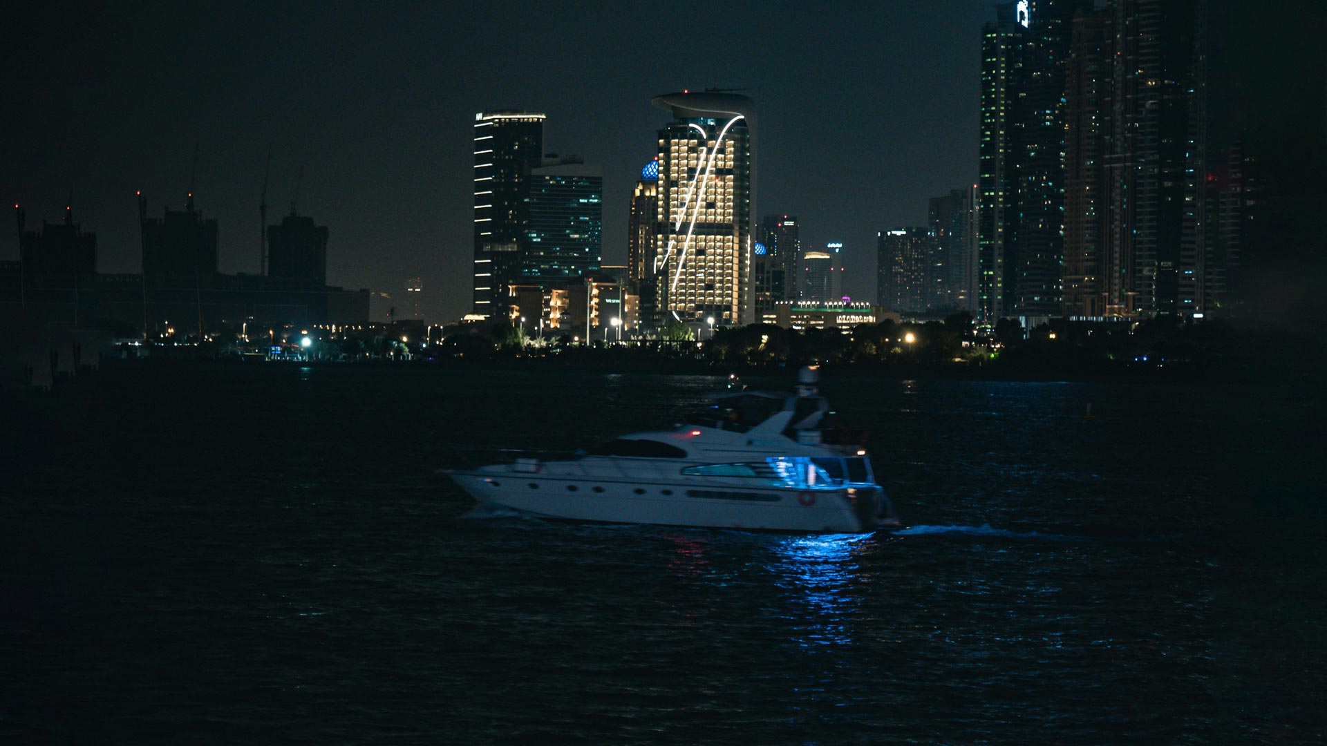 Yacht de plaisance naviguant de nuit face aux lumières de la ville, idéal pour le camping nautique sur le Bassin d’Arcachon